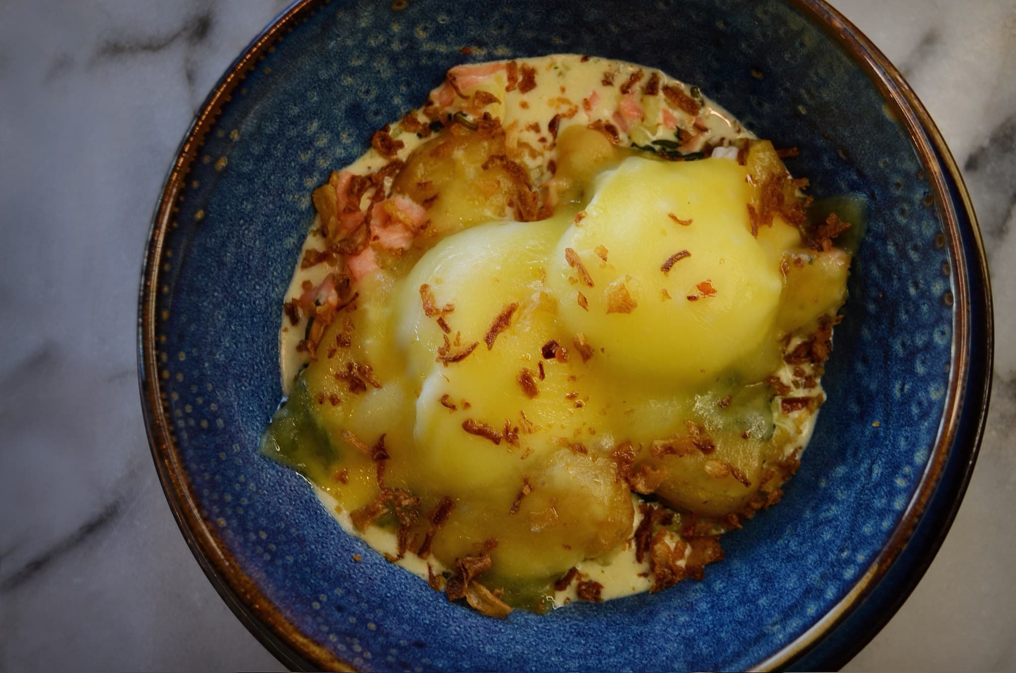 Smoked salmon hot pot with poached eggs and melted cheese sauce, finished with crispy onion